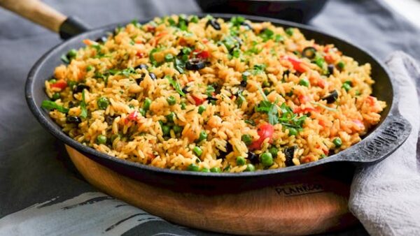 Colorful vegetable fried rice served in cast iron pan with fresh herbs, ideal for food photography.